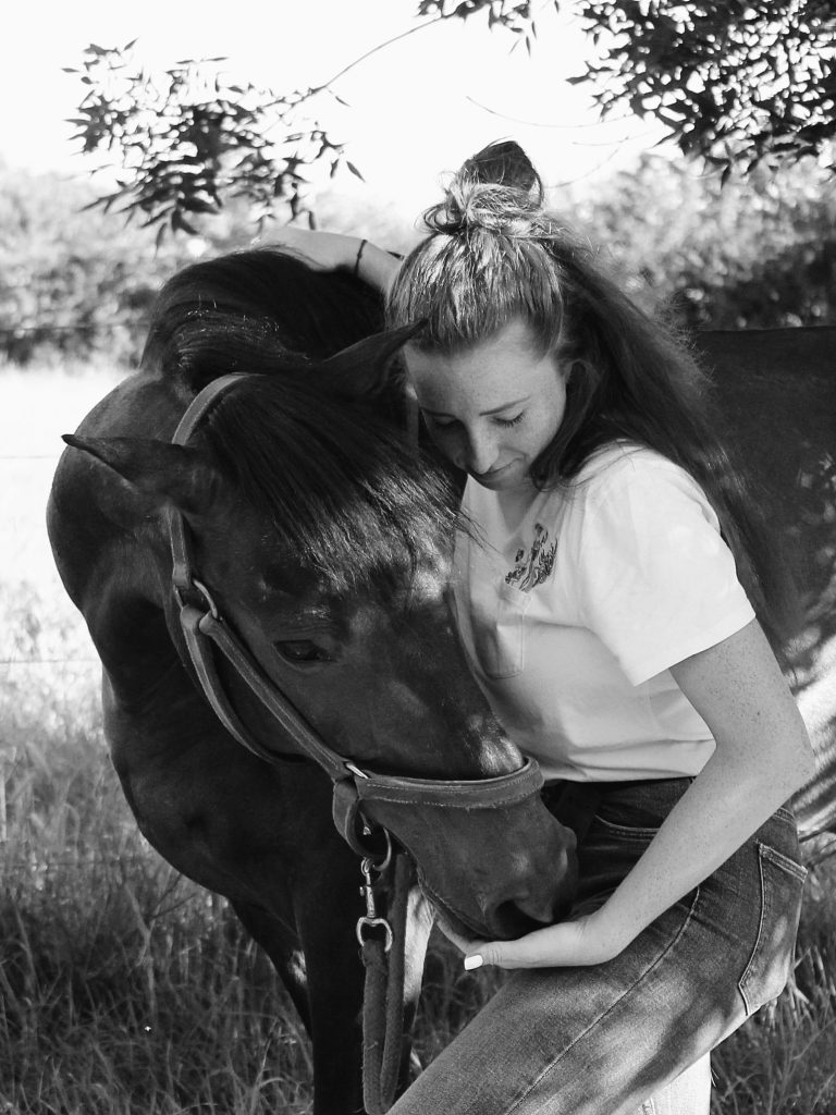 Photo en noir et blanc d’un cheval lors d’une consultation ostéopathique avec sa praticienne zoé gorli. Abord du cheval avec la tête tournée vers la gauche pour pourvoir sentir les vertèbres cervicales
